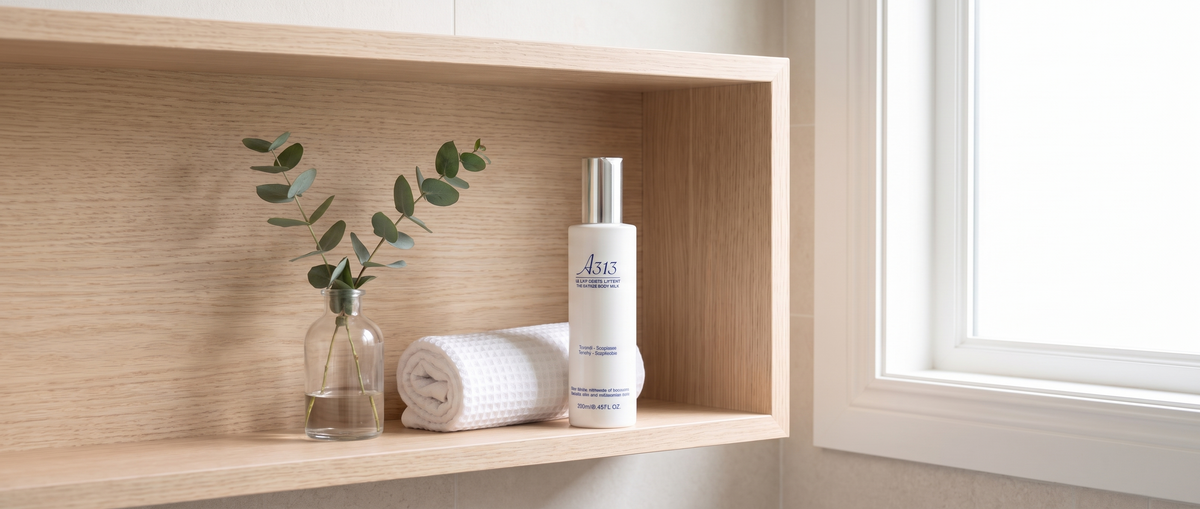 Fles A313 Lifting Body Milk op een lichthouten badkamerplank naast een opgerolde witte handdoek en een takje eucalyptus