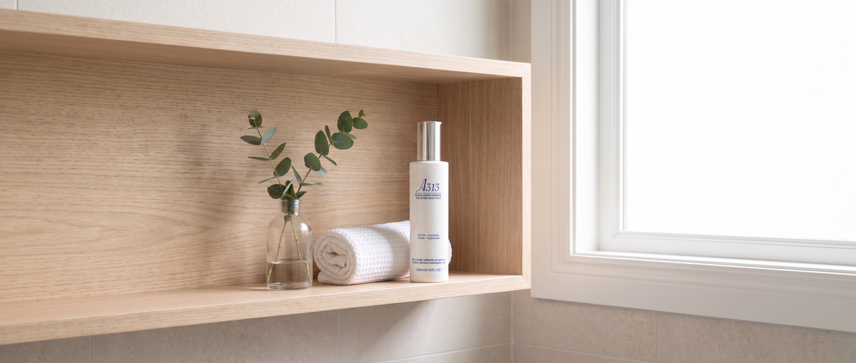 A313 Body Lifting Cream bottle on a pale-wood bathroom shelf beside a rolled white towel and a sprig of eucalyptus